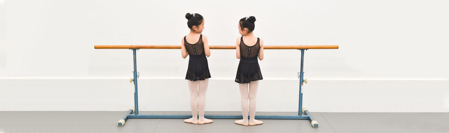 two girls standing infront of a ballet bar in first position